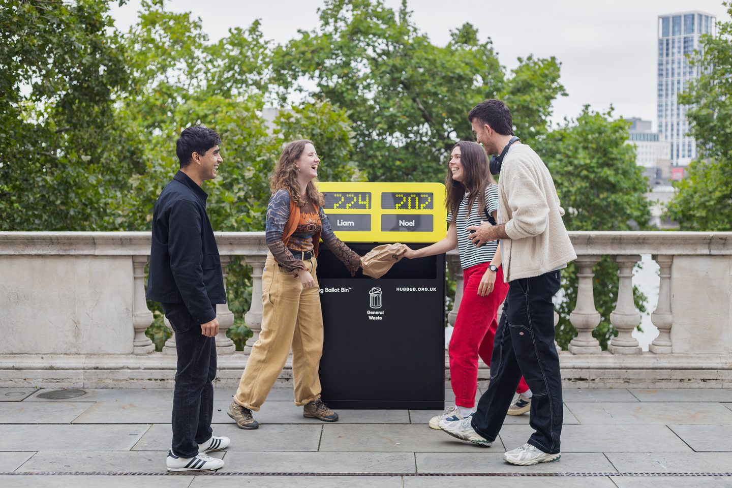 Four people standing around thee Big Ballot Bin, debating what to choose